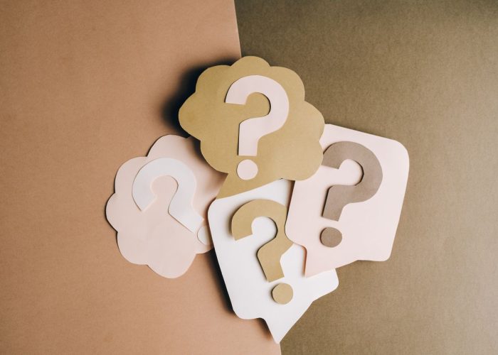 Question mark cutouts in layered paper craft style on a brown backdrop, conceptual art.